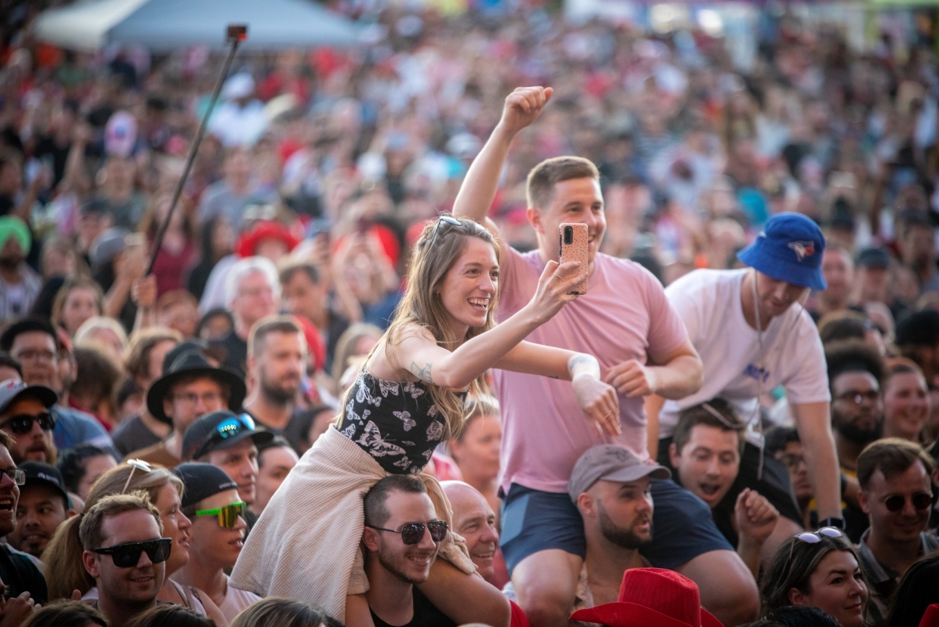 Festival audience with young woman and young men siting on their friends shoulders to view stage