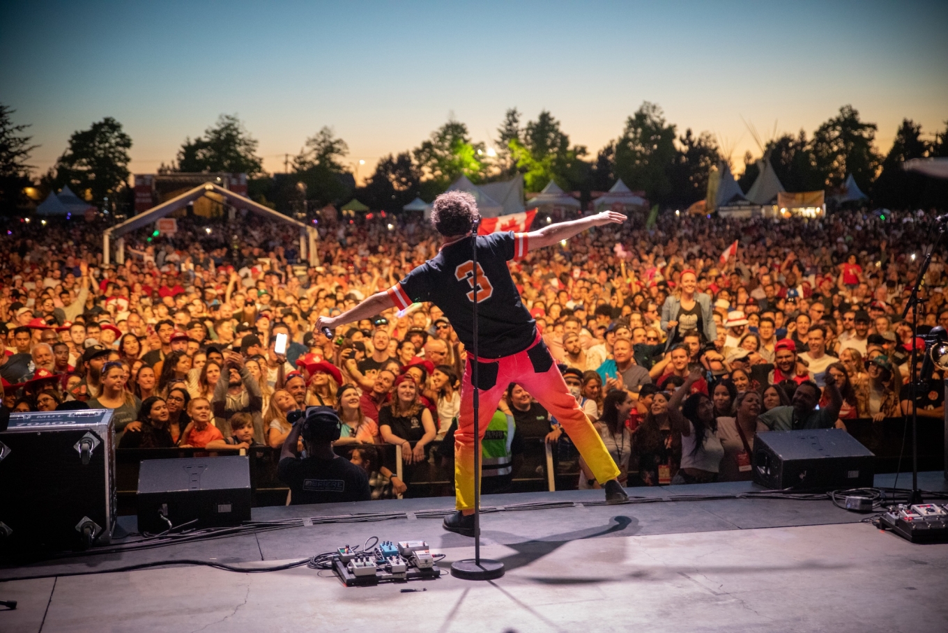 Performer on stage dances with outstretched arms facing large audience in background